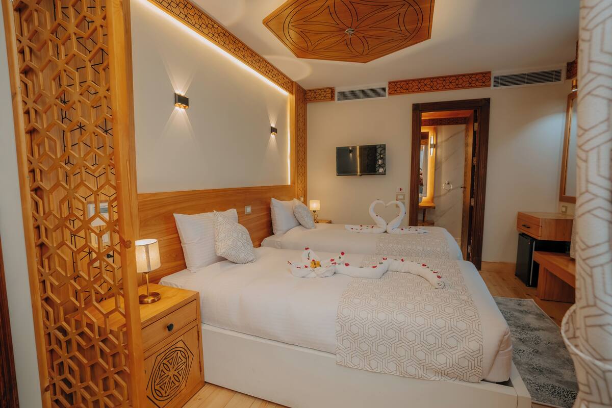 Ein Hotelzimmer mit zwei Betten, einem hölzernen Kopfteil, einem an der Wand befestigten Fernseher und einer Holzwand mit geometrischem Muster.