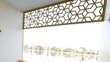 A balcony with two wooden chairs and a bench, overlooking a calm body of water with buildings in the background.