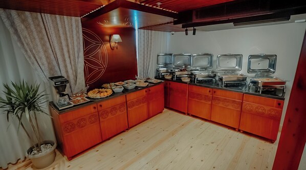 A kitchen with wooden cabinets, a coffee machine, and a buffet setup with multiple serving dishes. - Azhar Dahabiya Luxury Suites (Esna)