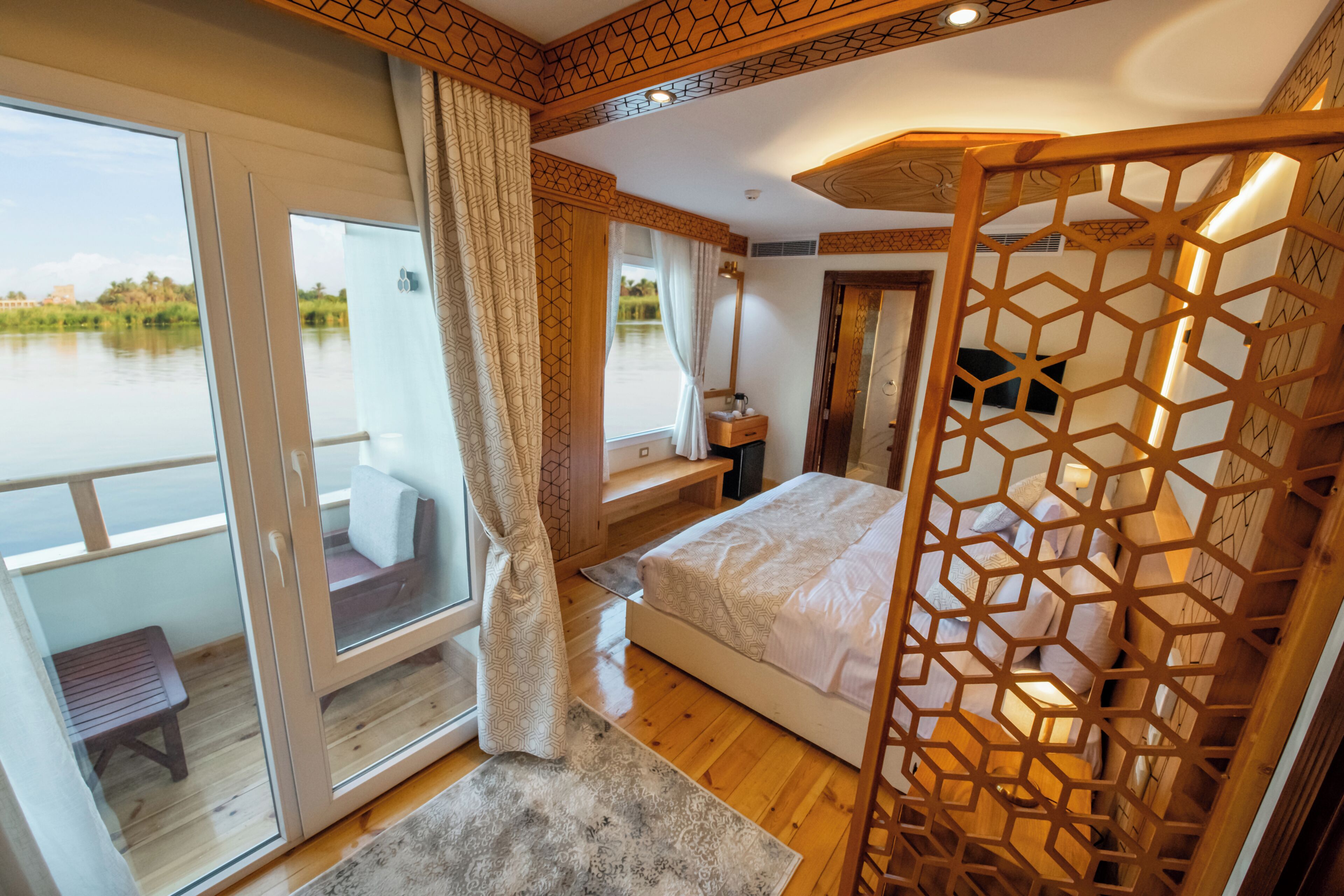 A bedroom with a large window, a bed, a wooden floor, and a view of a body of water.