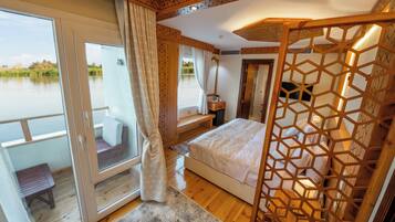 A bedroom with a large window, a bed, a wooden floor, and a view of a body of water.