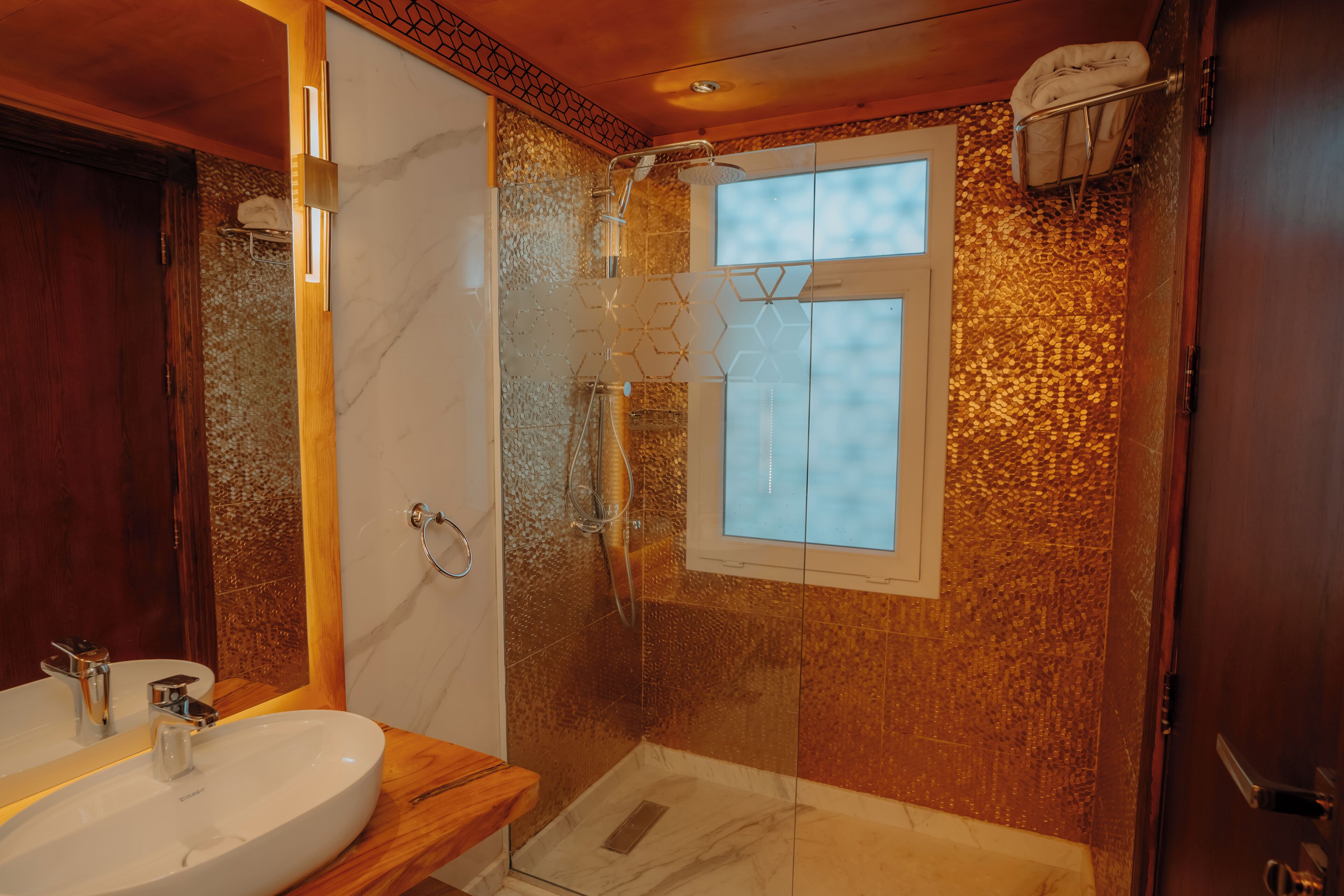 A bathroom with a wooden vanity, a glass shower enclosure, and a window.