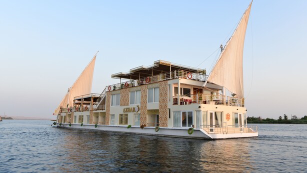 A large, multi-deck river cruise ship with a prominent name on the side, multiple decks with balconies, and lifebuoys along the side.