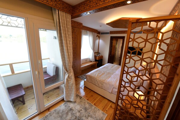 Un dormitorio con una cama grande, piso de madera, ventana con cortinas y vista al exterior.