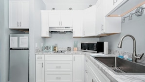 Una cocina moderna con armarios blancos, un lavamanos de acero inoxidable, un microondas y un refrigerador.