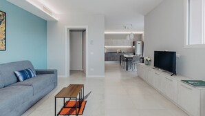 A modern living room with a grey sofa, a wooden coffee table, and a TV on a white cabinet. - Modern apartment with pool just steps from the beaches of Lake Garda (Padenghe Sul Garda)