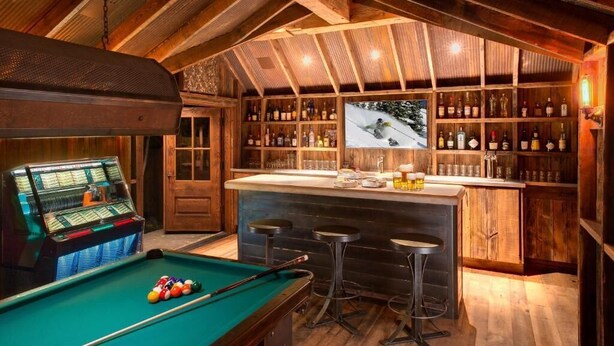 A pool table with billiard balls, a bar area with stools, and a shelf with bottles. - Eleven Sopris House (Crested Butte)