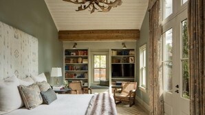 A bedroom with a large bed, bookshelves, a chair, and a door with curtains. - Eleven Sopris House (Crested Butte)