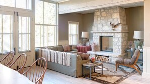 A spacious living room with a stone fireplace, a sofa, a dining table with chairs, and large windows. - Eleven Sopris House (Crested Butte)
