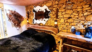 Ein rustikaler Raum mit Steinwand, einem hölzernen Bett und einem aufgehängten Tierfell.