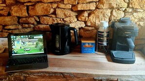 Ein Laptop, eine Kaffeemaschine und ein Kaffeezubereiter auf einem Holztisch vor einer Steinwand.