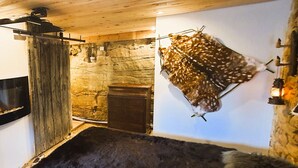Ein rustikaler Raum mit Steinwand, einem aufgehängten Fellstück, Kamin und Holzbalkendecke.