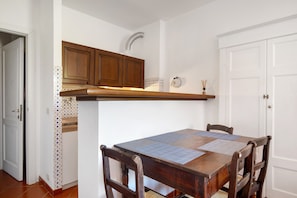 A dining area with a wooden table, chairs, and a kitchen with wooden cabinets and a white door.