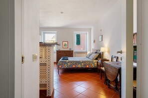 A bedroom with a bed, a desk, a chair, a radiator, a window, and a door.