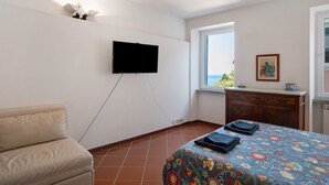 A bedroom with a bed, a television mounted on the wall, a window with a view, and a wooden dresser.