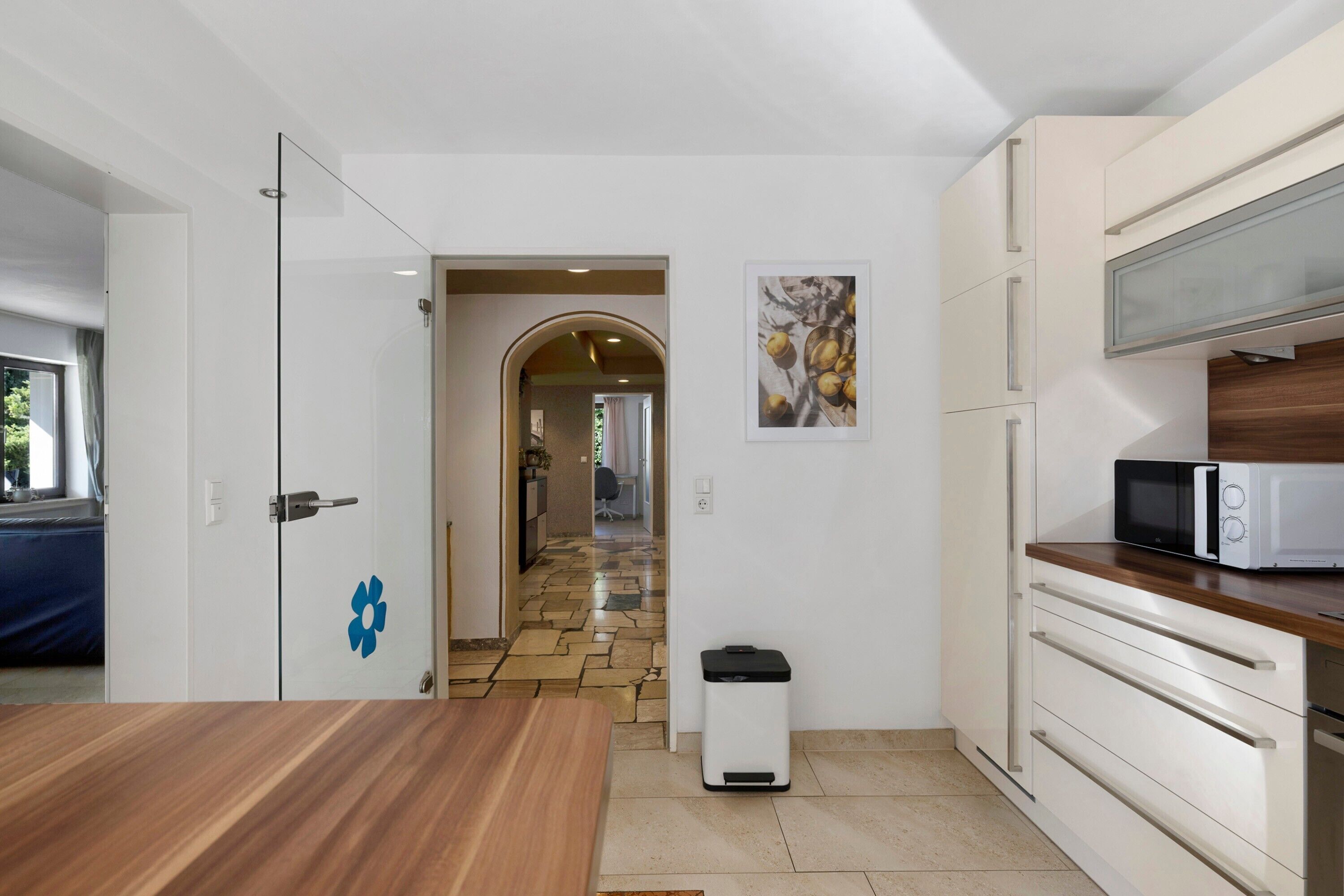 Een moderne keuken met witte kastjes, een magnetron en een vuilnisbak.