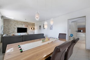 A modern living room with a wooden dining table, a grey sofa, and a TV mounted on a brick wall. - Apartment 'Mayer' with Private Terrace, Shared Garden and Wi-Fi (Albstadt)