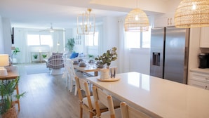 A modern kitchen with a large island, stainless steel appliances, and wicker pendant lights. - Gulf-Front Luxury! Regency 501 – Modern Remodel + Incredible Views (Panama City Beach)