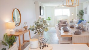 A dining area with a wooden table set for four, surrounded by white chairs. A mirror hangs on the wall to the left, and a plant is placed on the table. - Gulf-Front Luxury! Regency 501 – Modern Remodel + Incredible Views (Panama City Beach)