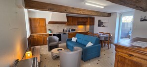 A compact living space with a kitchenette, a blue sofa, a dining table, and a wooden ceiling.