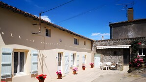 A building with a tiled roof, a stone wall, and a paved courtyard with potted plants. - Holiday Home for 4 "La Marguerite" Countryside Gite near Puy du Fou (Les Herbiers)