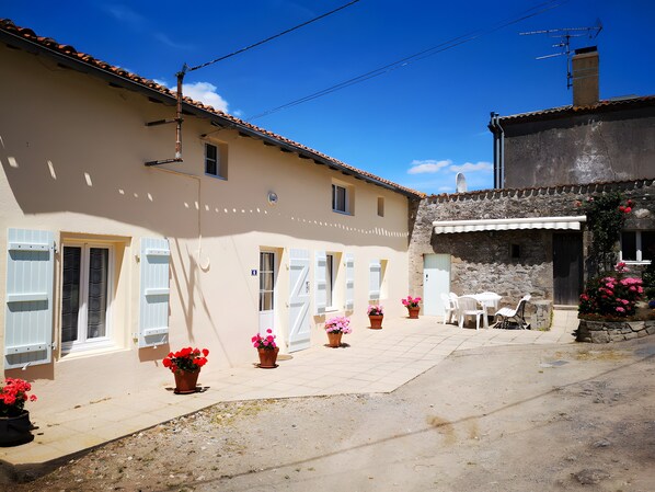 A building with a tiled roof, a stone wall, and a paved courtyard with potted plants.