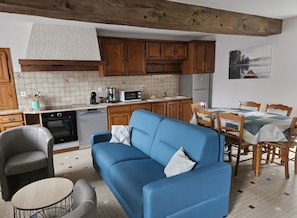 Une cuisine moderne avec des meubles en bois, un coin repas avec une table et des chaises, un canapé bleu et une petite table ronde.