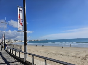 Une plage avec une promenade, un ciel dégagé et une vue lointaine sur la ville.
