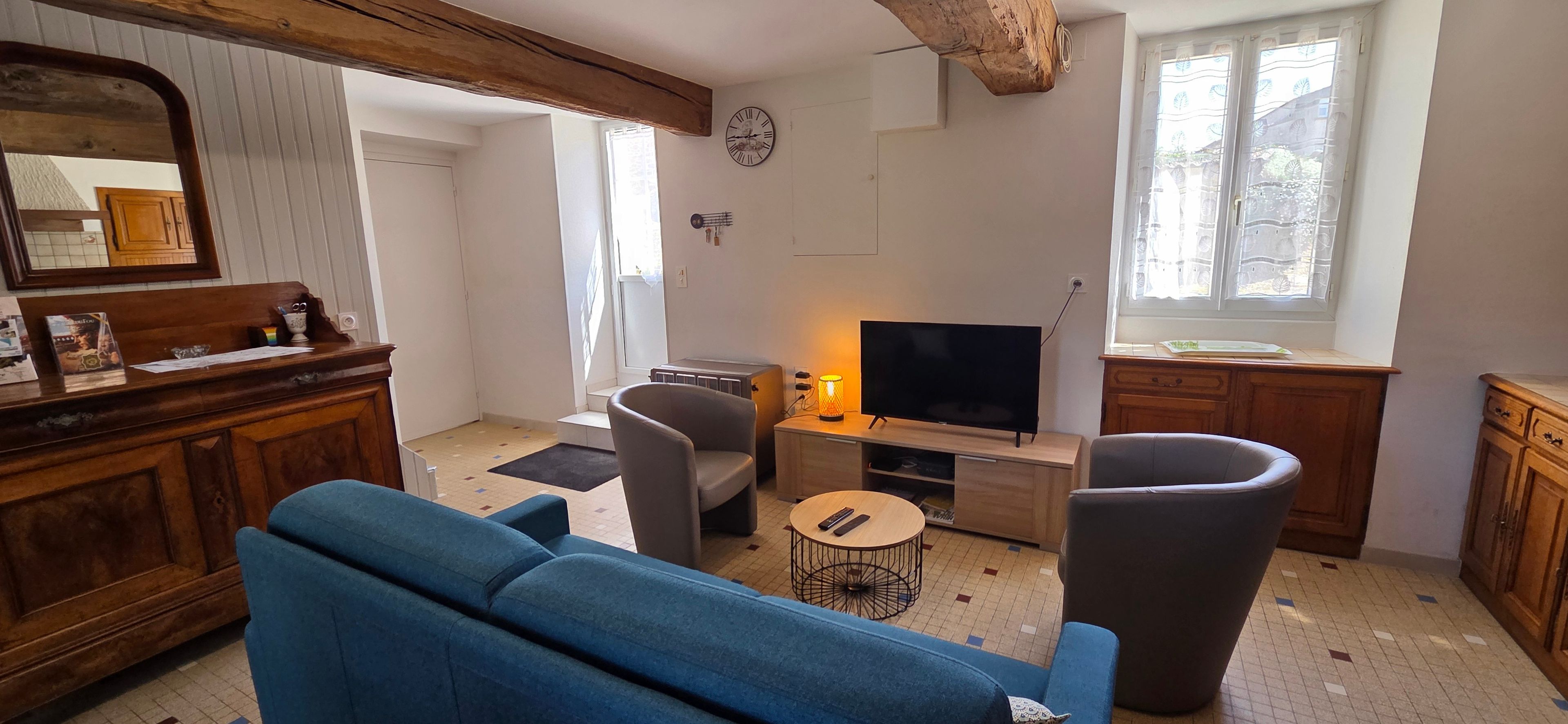 Ein Wohnzimmer mit einem blauen Sofa, einem grauen Sessel, einem kleinen runden Tisch, einem Fernseher und Holzschränken.