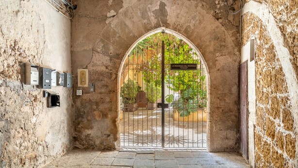 Un arco de entrada con una reja de metal, suelo de piedra y un letrero que dice "LA RESIDENZA DEL REGINALE".