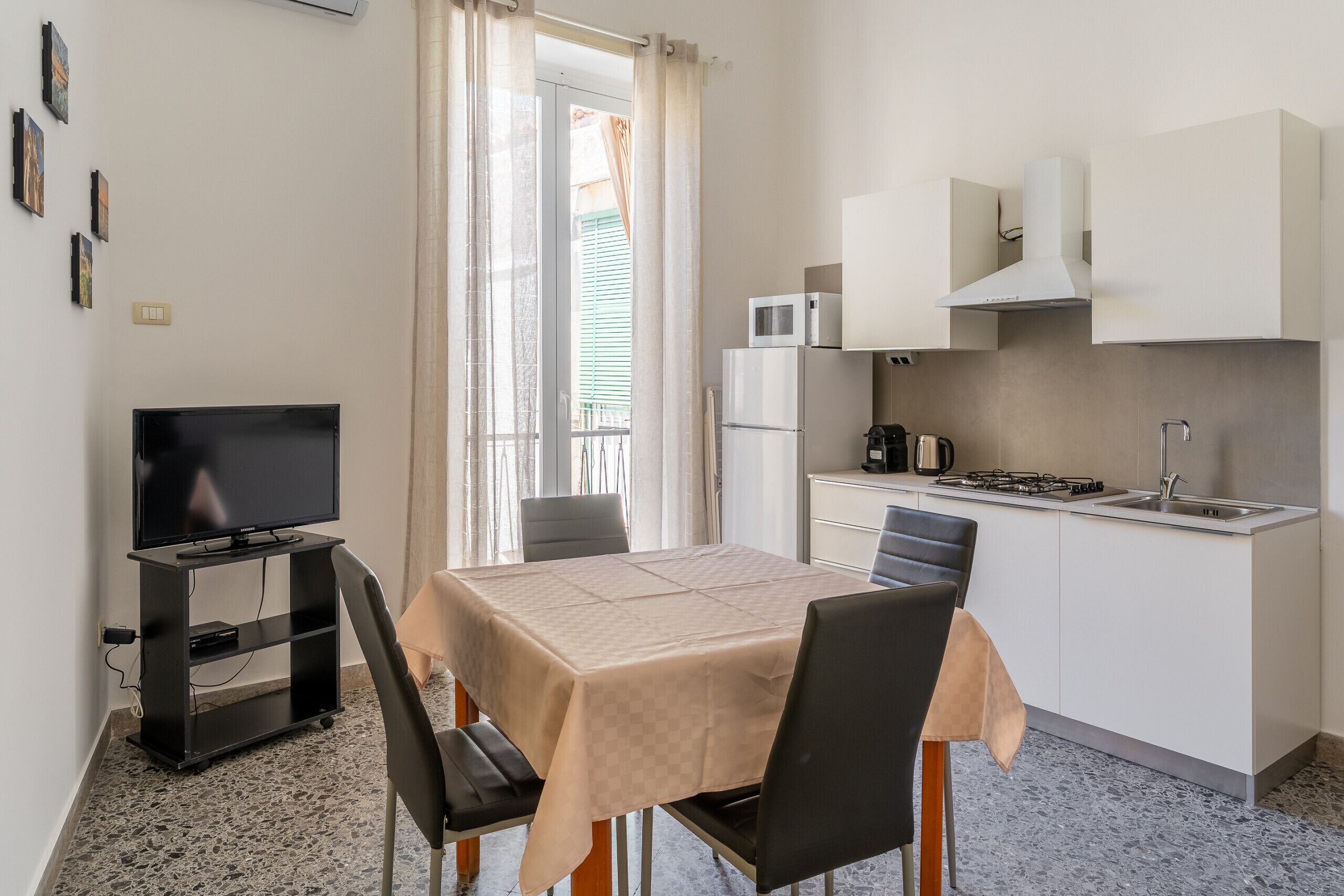 A compact kitchen with a dining table, chairs, a TV on a stand, a microwave, and a sink.