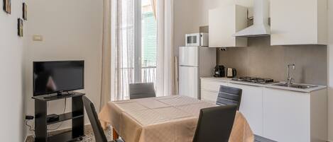 A compact kitchen with a dining table, chairs, a TV on a stand, a microwave, and a sink.
