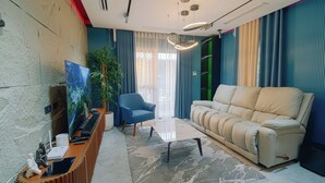 A modern living room with a beige sofa, a blue armchair, a flat-screen TV, a coffee table, and a large window with curtains. - Executive 2-bedroom condo in Subic Bay Freeport Zone (Subic Bay Freeport Zone)