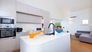 Una cucina moderna con mobili bianchi, forno a incasso e un'isola grande con un lavello. Sull'isola c'è una ciotola di frutta e due bicchieri di succo d'arancia sul bancone.