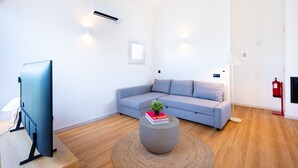 Una sala de estar moderna con un sofá gris, una mesa redonda de centro con un libro y una planta, un televisor de pantalla plana y un extintor de incendios rojo.