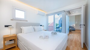 Ein modernes Hotelzimmer mit einem großen Bett, einem Nachttisch, einer Lampe und Blick auf den Balkon.