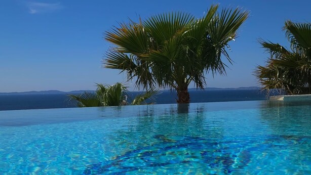 Una piscina infinita con agua azul cristalina, rodeada de palmeras y vista al mar.