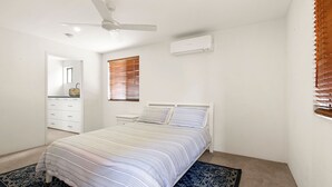 Et soveværelse med seng, ventilator, aircondition, et vindue med rullegardiner og en kommode.