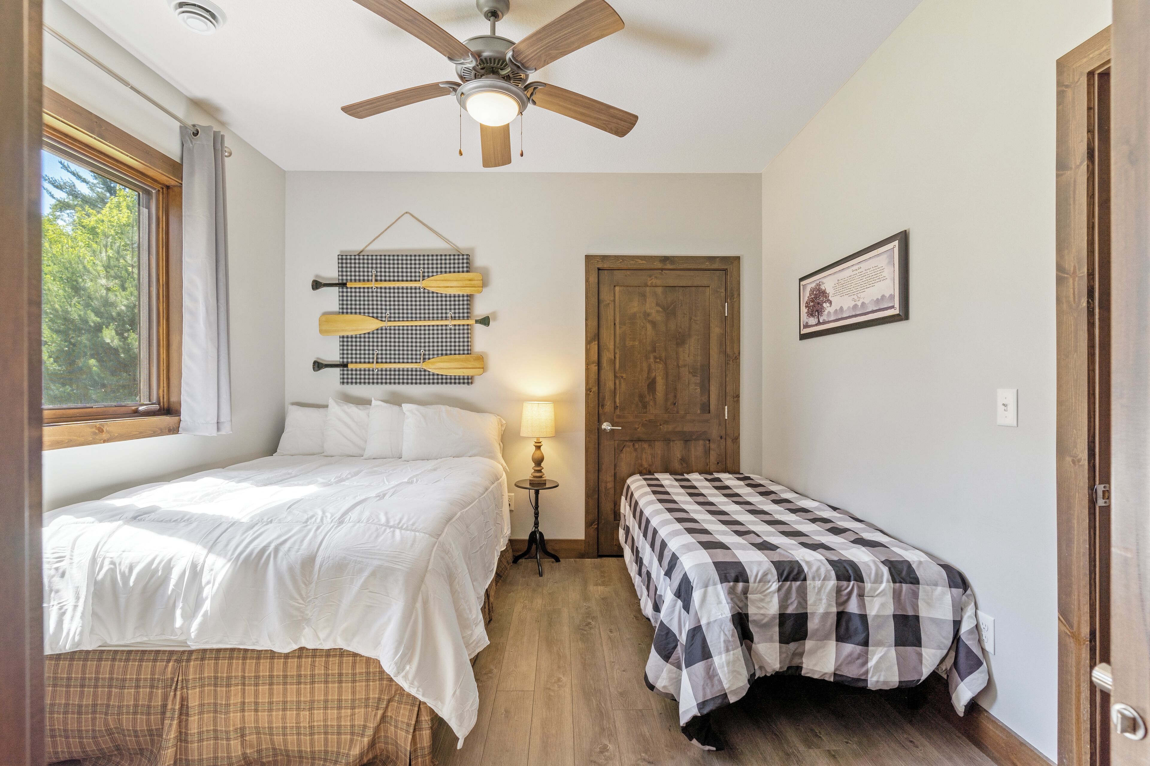 A bedroom with two beds, a ceiling fan, a wooden door, and a window with curtains.