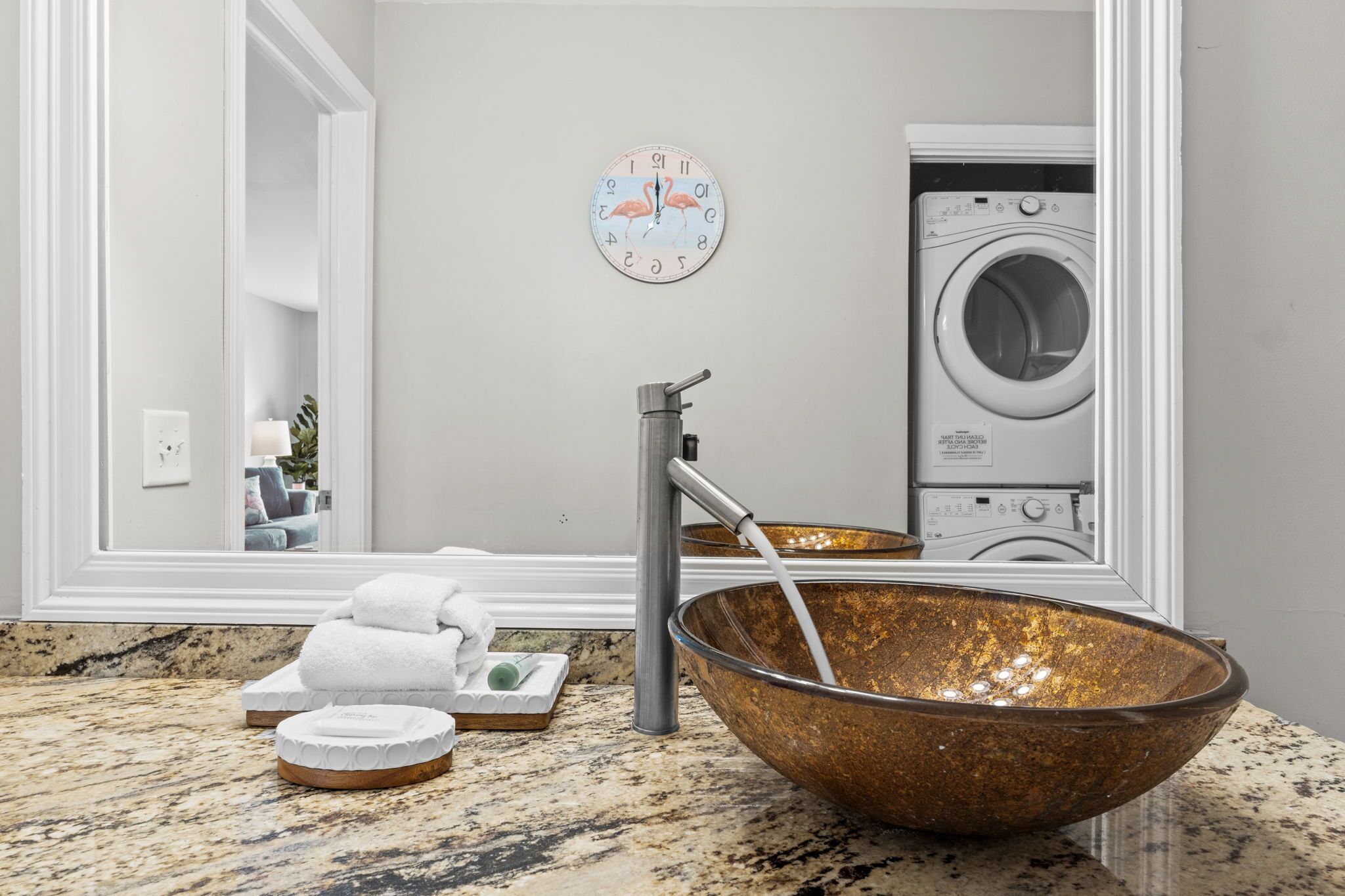 A bathroom with a large mirror, a sink with a copper bowl, a faucet, and a washing machine in the background.