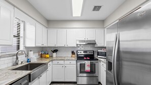 A modern kitchen with white cabinets, stainless steel appliances, a double sink, and a tiled backsplash. - The Pink Flamingo by Book That Condo (Panama City Beach)