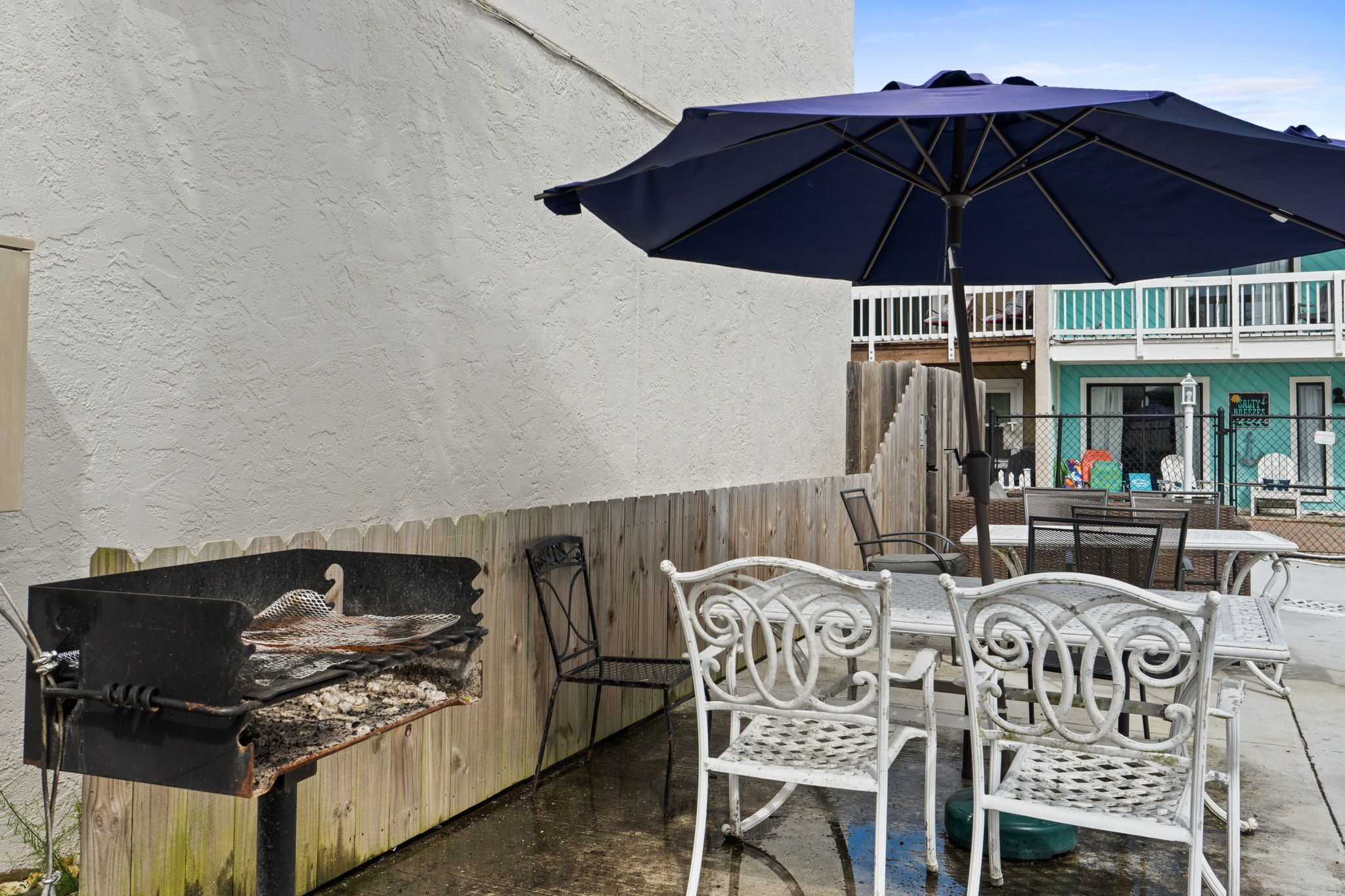 Une terrasse extérieure avec un barbecue, des chaises en métal blanches et un grand parasol.