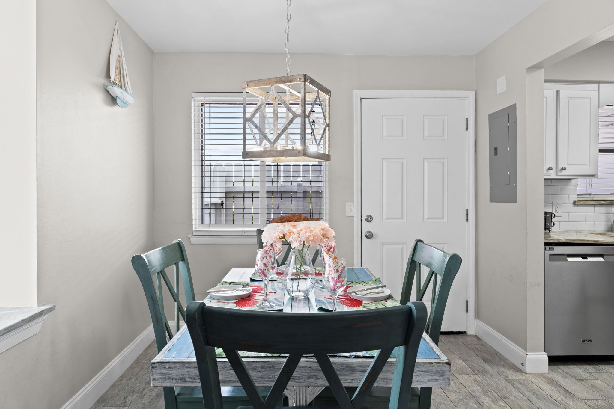 A dining area with a round table, four chairs, a hanging light fixture, and a window with blinds.