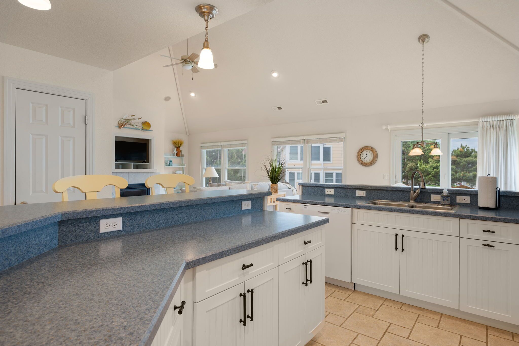 A kitchen with white cabinets, a blue countertop, and a window with a view of greenery.