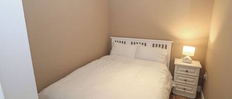 A small, neatly made bedroom with a single bed, a bedside table with a lamp, and a radiator.