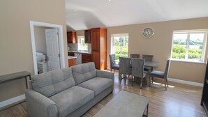 Un salon moderne avec un canapé gris, une table à manger avec quatre chaises et un coin cuisine doté de meubles en bois et d’une fenêtre.