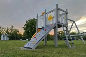 A playground with a slide and climbing wall, surrounded by grass and trees. - Family Holiday Homes, Playground, Summer Pool (Ustronie Morskie)
