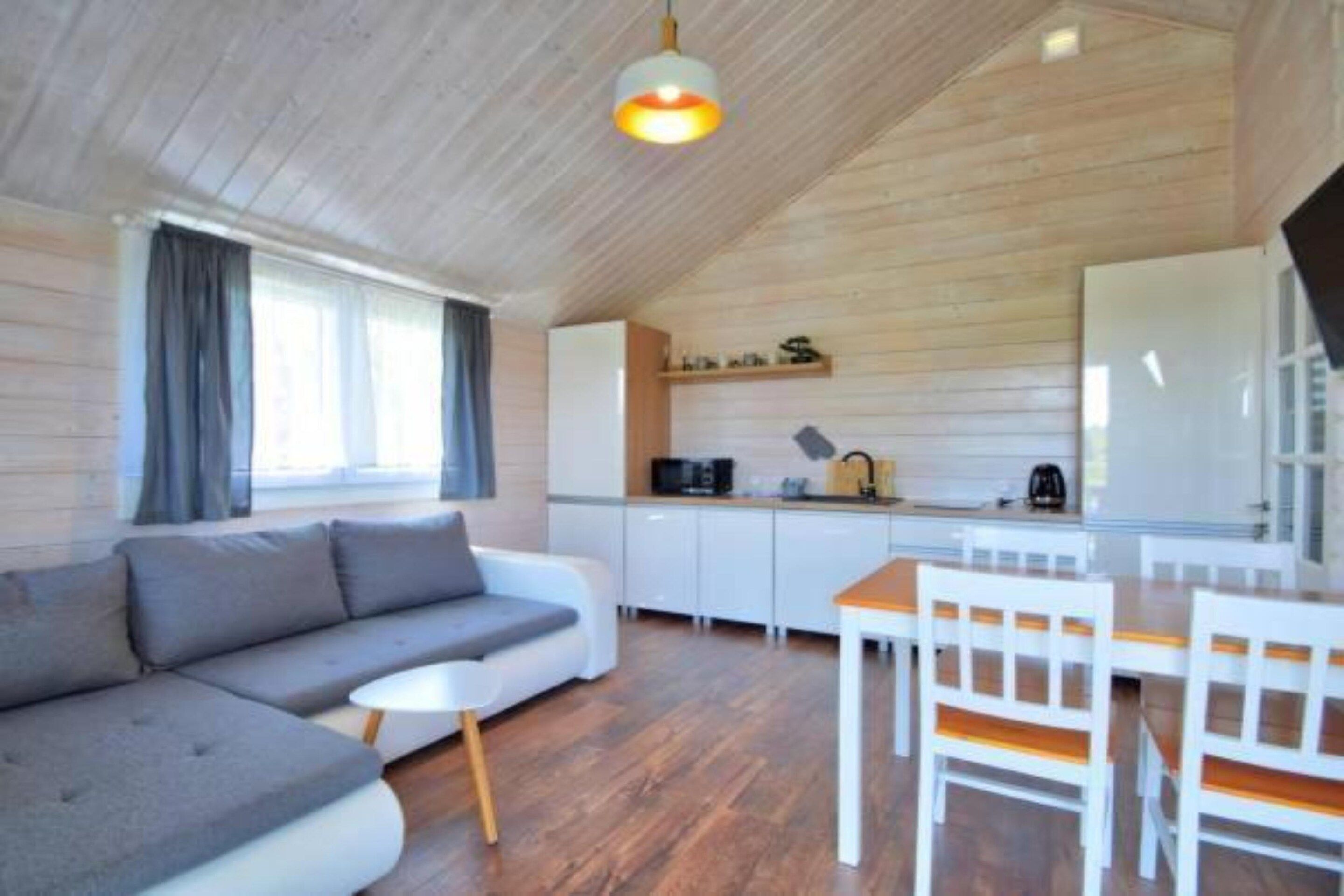 A cozy living area with a sofa, a dining table with chairs, a kitchen with white cabinets, and a wooden ceiling.