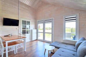 A room with a wooden ceiling, a television mounted on the wall, a dining table with chairs, a sofa, and large windows with blinds. - Family Holiday Homes, Playground, Summer Pool (Ustronie Morskie)