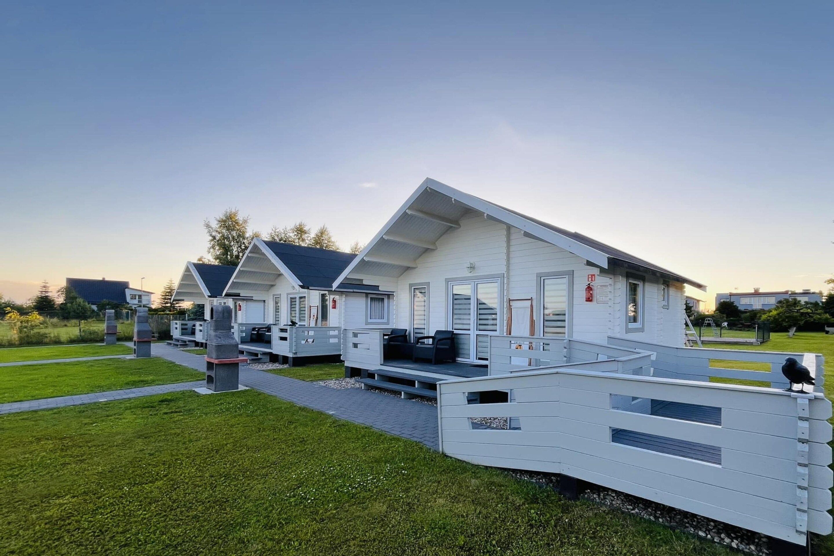 A row of modern, white mobile homes with flat roofs and large windows, arranged in a row on a grassy area with a clear sky.